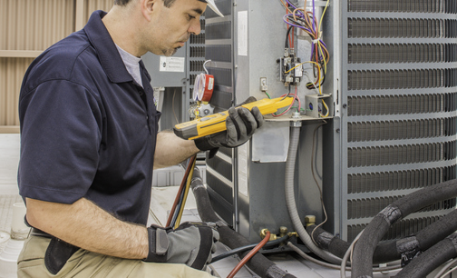 Trained hvac technician holding a voltage meter, performing preventative maintenance on a air conditioning condenser unit. | Advanced Heating and Air Conditioning